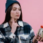 Pensive woman with a savings jar labeled 'where to next' on a pink background.