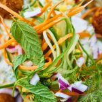Vibrant salad featuring fresh vegetables, falafel, and herbs in a white bowl, perfect for a healthy meal.